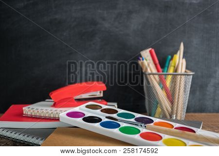 Angled View Over A Wooden Desk With School Supplies On It. Stepler, Colored Pencils, Notebooks, Calc