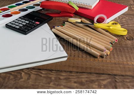 Angled View Over A Wooden Desk With School Supplies On It. Stepler, Colored Pencils, Notebooks, Calc