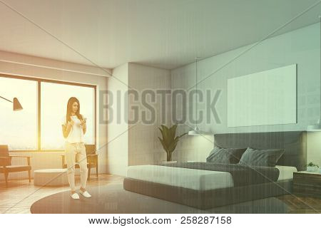 Woman Looking At Phone In Minimalistic Bedroom With Round Carpet, Masterbed, Night Stand And Round C