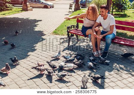 Young Mixed Race Couple In Love Feeding Bidrs In Summer Park. Man And Woman Thowing Bread To Doves