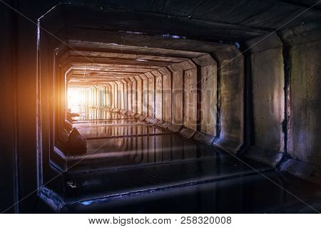 Flooded Sewer Tunnel Is Reflecting In Water. Dirty Urban Sewage Flowing Throw Rectangular Sewer Tunn
