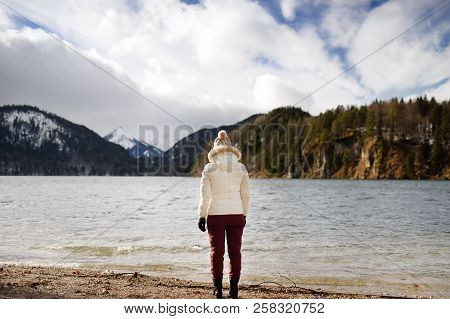Feamle Tourist Enjoy Wonderful Winter View Of Lake Alpsee, Located Near Hohenschwangau And Neuschwan