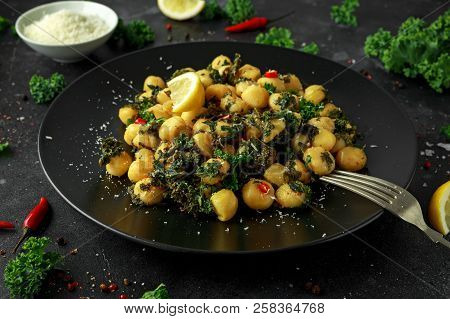 Fried Kale And Potato Gnocci With Chilie, Peccorino Cheese And Lemon Wedges In Black Plate. Italian 