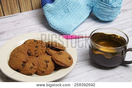 A Plate Of Choco Chips Cookies, A Cup Of Green Tea, And Crocheting Project