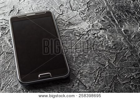 The Phone Is On A Dark, Heterogeneous Background. Black, Brown, Gray, Color.