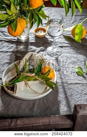 Table Setting With White Plate, Cutlery, Linen Napkin And Orange Tree Branch Decoration On Gray Line