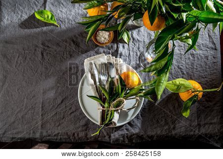 Table Setting With White Plate, Cutlery, Linen Napkin And Orange Tree Branch Decoration On Gray Line