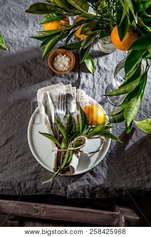 Table Setting With White Plate, Cutlery, Linen Napkin And Orange Tree Branch Decoration On Gray Line