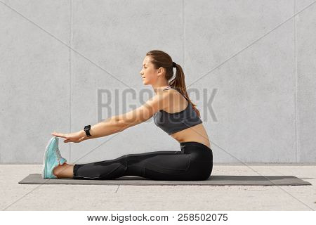 Photo Of Motivated Girl Does Stretching Workout Or Acrobatics Exercises On Fitness Mat, Recieves Yog