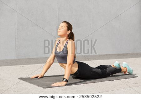 Photo Of Pleasant Looking Sporty Woman With Healthy Skin, Keeps Eyes Shut, Dressed In Casual Sportsw