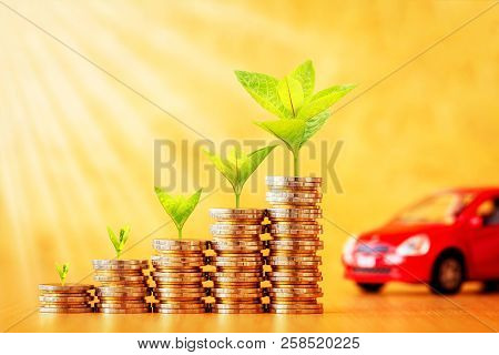 Stack Coin With Plant Growing On The Top For Collect Interest And Red Car Put On The Desk In The Off