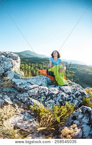 A Woman Is Sitting In A Sleeping Bag On Top Of A Mountain. A Smiling Girl Rests After A Climb. The B