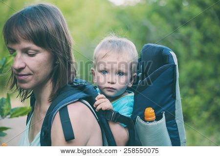 A Boy Is Sitting In A Backpack. The Kid Is Traveling With His Parents. Climbing With A Child. The Mo