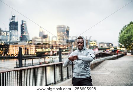 Black Man Runner With Smartphone In An Armband On The Bridge In London, Resting.
