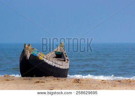 A Lonely Boat Lying Stable On The Sea Shore Beach With Waves In Blurry Background.