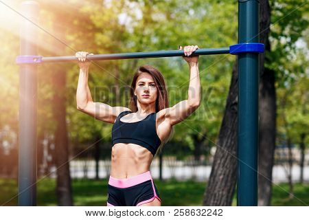 Girl On Street Workout. Woman Pull-ups Herself Up On Bar On Sports Ground In Park.