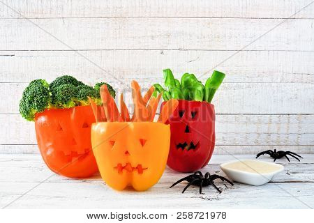 Healthy Halloween Food. Vegetables And Dip In Jack O Lantern Bell Peppers. Side View Against White W