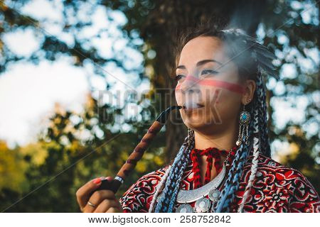 Beautiful Young Girl In A Dress Of Native Americans Smoking Pipe, Close Up