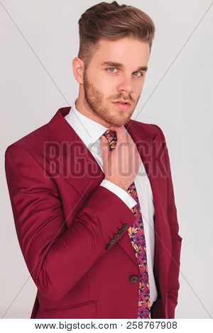portrait of a sexy young businessman fixing his tie's knot , studio picture on grey background