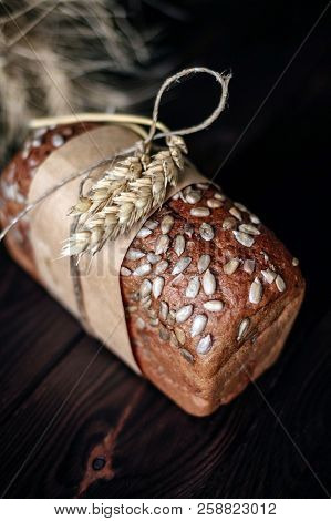 Rye Bread Wrapped In Parchment And Wheat On A Dark Wooden Photophone