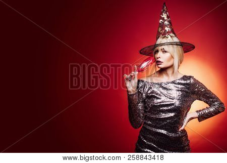 Gelightful Blonde Lady With A Glass Of Champagne On Red Background. Beautiful Surprised Woman In Wit