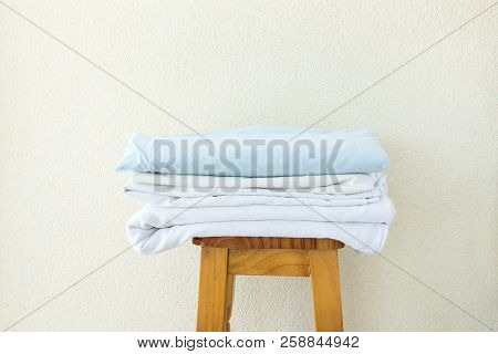 Stacked Clean Folded Cotton Bedlinen On Wooden Stool White Wall Background. Laundry Washing Cleanlin