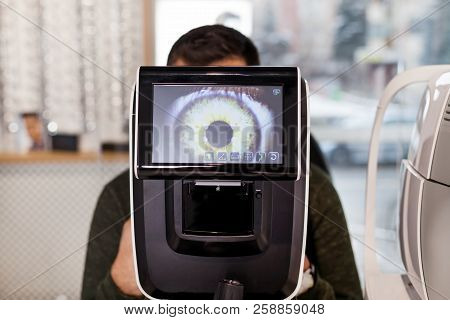 Ophthalmologist Examining Young Man With Optometric Machine In Optics Store
