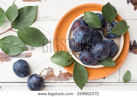 Fresh Plum Berries On A Plate With Leaves On A Light Table.
