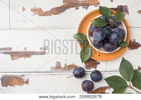 Fresh Plum Berries On A Plate With Leaves On A Light Table.