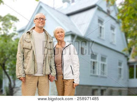 old age, accommodation and real estate concept - happy senior couple holding hands over living house background