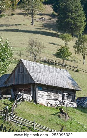 The Old Ukrainian Hut With A Slate Roof And A Wooden Fence In A Green Field