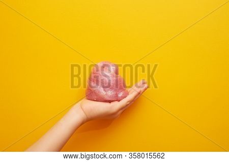 Pink Slime With Sequins, In A Childs Hand, On A Yellow Background. Creativity, Creativity And Experi