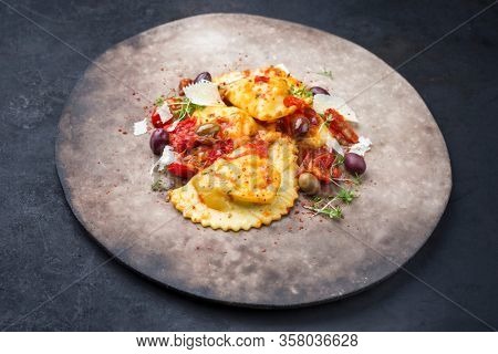 Traditional Italian ravioli pasta offered with parmesan cheese, fried tomatoes and olives as closeup on a modern design plate with copy space 