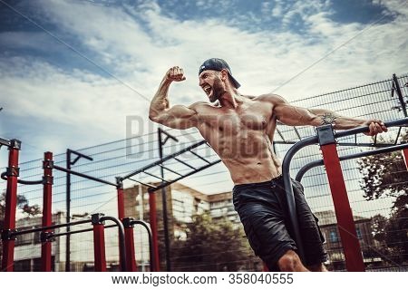 Bearded Bodybuilder Man Exercising On Monkey Bars For The Upper-body In A Modern Calisthenics Park O