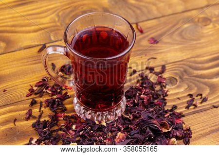 Glass Cup Of Red Hibiscus Tea (carcade, Roselle) On Wooden Table