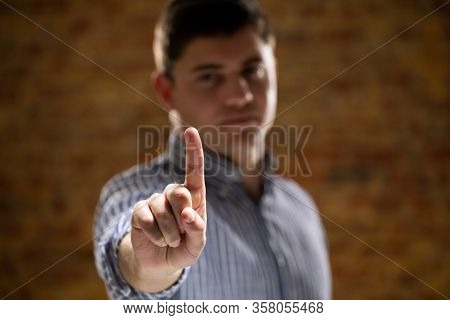 Front view of a Caucasian man with short hair wearing a checked shirt with arm raised and hand out in front of him, with his index finger facing camera, touching a virtual interactive screen.