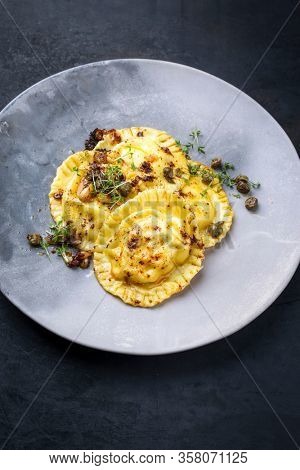 Traditional Italian ravioli pasta offered with capers and onion chili pesto closeup on a modern design plate with copy space