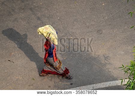 New Delhi, India - March 21, 2020: Indian Woman Wearing A Sari Walks While Carrying And Balancing A 