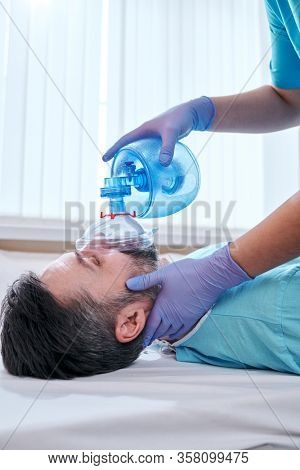 Close-up of nurse doing pulmonary ventilation with Ambu bag mask to mature patient with coronavirus