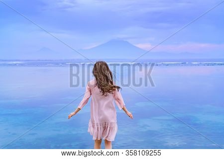 A Elegant Young Brunette Girl In A Pink Dress Blown By The Wind Running Towards The Ocean And Mounta