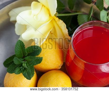 Red Orange Juice O Grapefruit Juice In A Glass On Steel Plate With Mint Leaf, Lemons And Yellow Rose