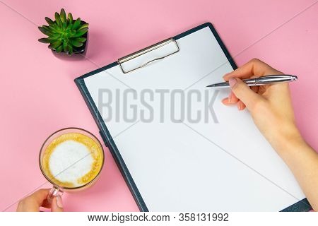Tablet With White Flattery Next To Which Stands A Green Plant, Hand Holds A Pen And Writes On A Shee