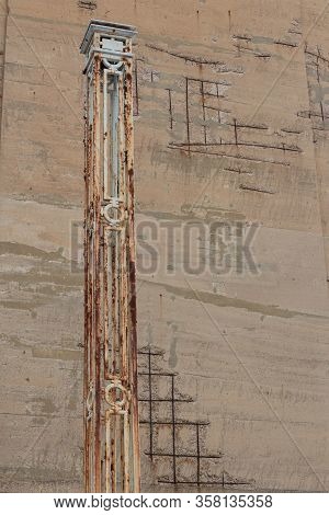Tall Wrought Iron Post With Rust And Gray Paint Against A Crumbling Concrete Wall Face With Exposed 
