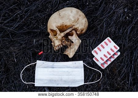 A Human Skull On A Black Background Of Burnt Grass With Red Capsules Of Medical Drugs. A Symbol Of H