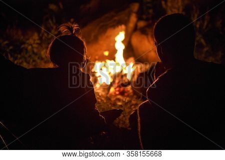 My Daughter And Father Sit By The Fire At Night On A Picnic In Nature. Black Silhouettes Of A Family