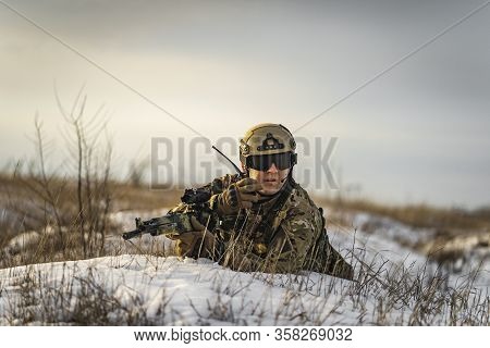 Modern War Soldier Army Man In Multicam Camouflage Is Lying In Winter Field And Speaks On The Walkie