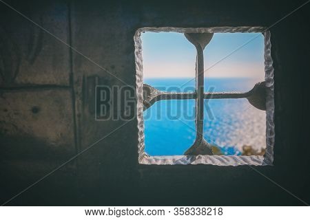 Old Wrought-iron Black Door And A Metal Grating On The Window With A View Of The Blue Sea Outside, T