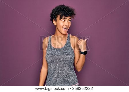 Young beautiful african american afro sportswoman doing exercise wearing sportswear smiling with happy face looking and pointing to the side with thumb up.