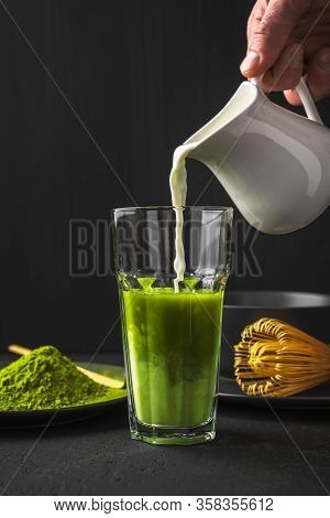 Matcha Green Tea Powder Latte With Milk In Two High Glass On Stone Table, Process Of Pouring Milk In