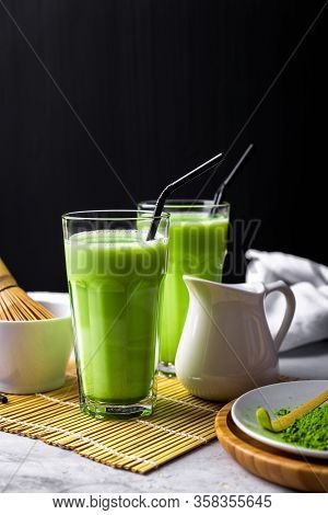 Matcha Green Tea Powder Latte With Milk In Two High Glass On Stone Table, Black Straw, Wooden Plate 